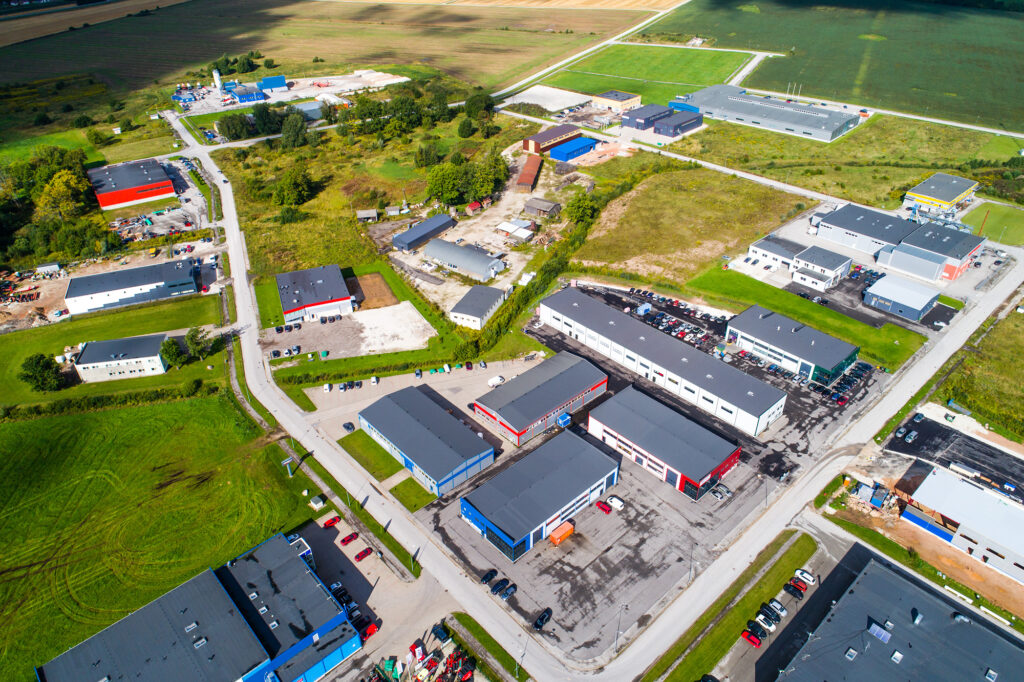 Linnulennult tehtud diagonaalne foto, kus reas mitu erinevat värvi (punased, sinised, hallid) ladu-angaarid, taustal põllud ja metsatukk.
